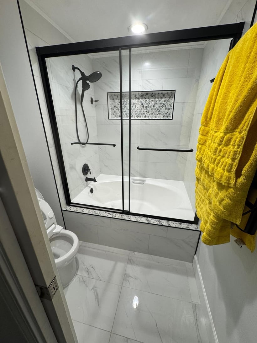Finished bathroom shower with black framed glass doors and light tile walls