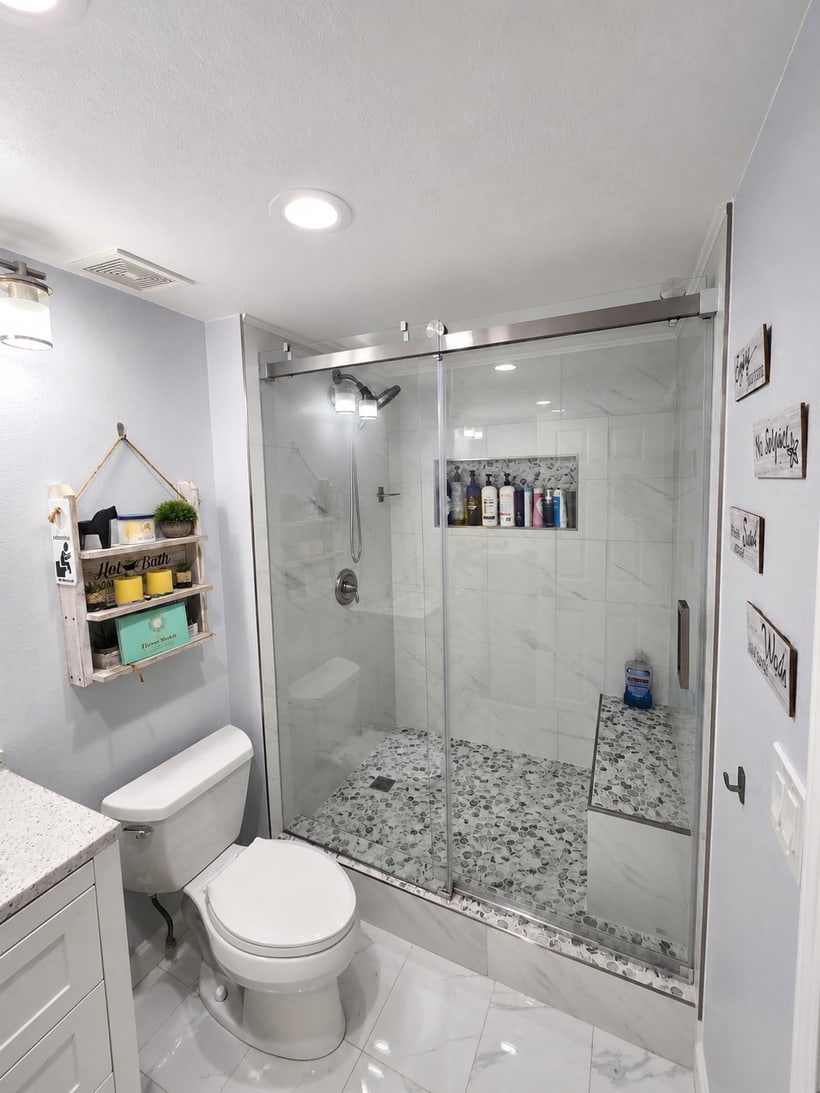 Bathroom remodel with glass sliding shower doors, marble-look wall tile, pebble shower floor, built-in niche, and bench